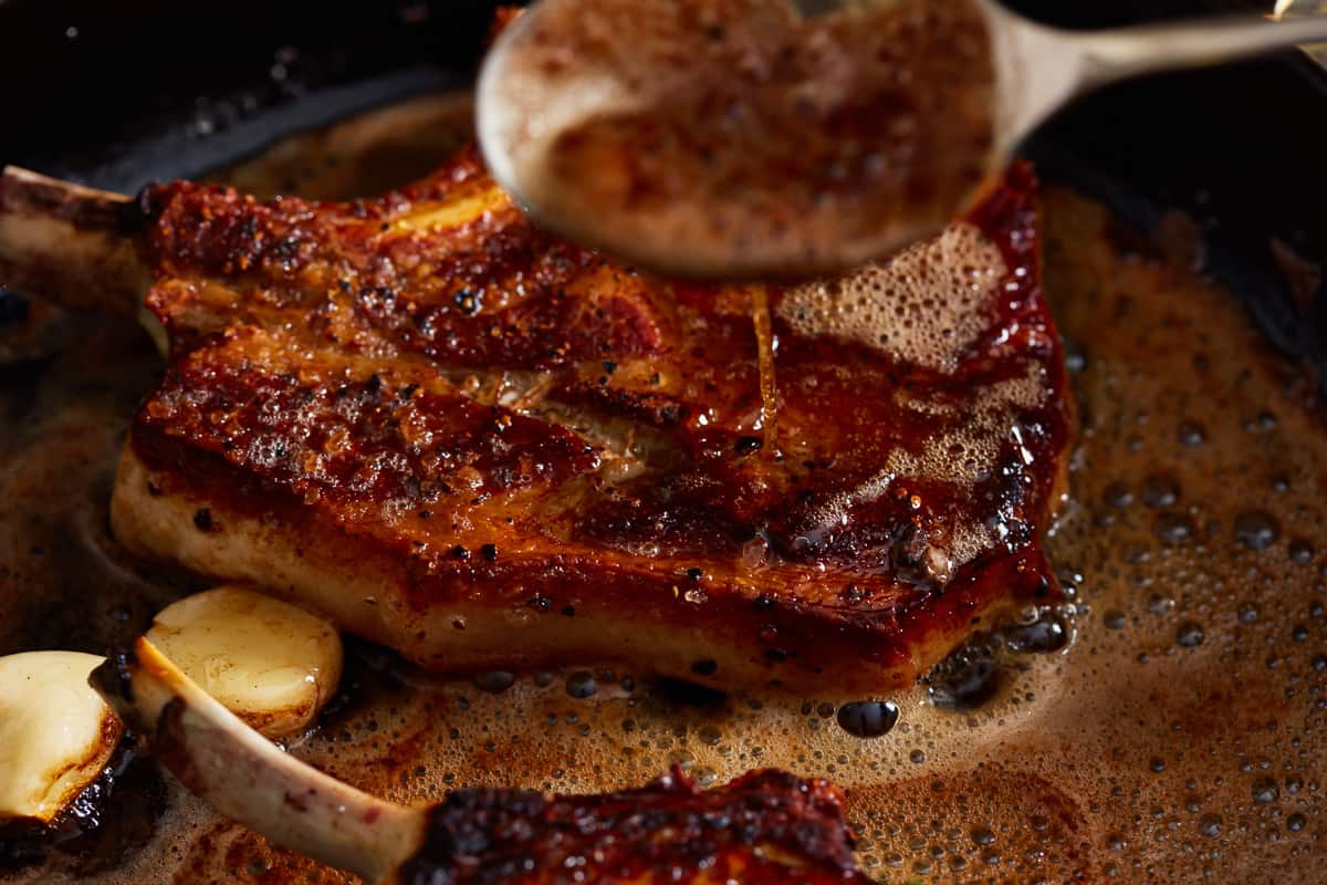 spooning butter over seared pork chops in a pan.