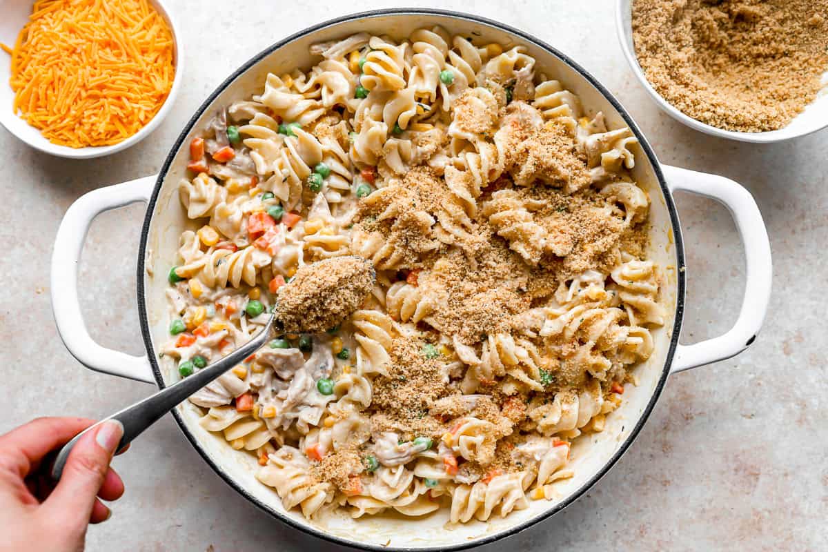 sprinkling breadcrumbs over chicken noodle casserole in a pan.