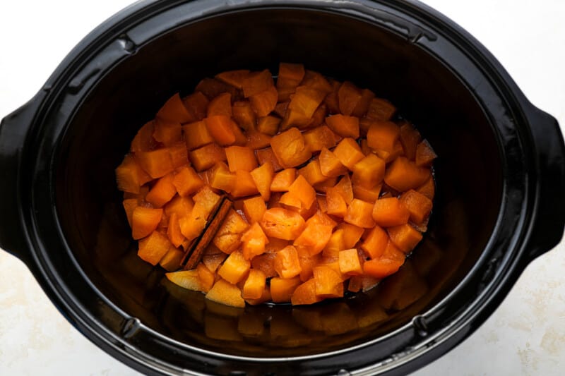 cooked chopped apples and a cinnamon stick in a crockpot.