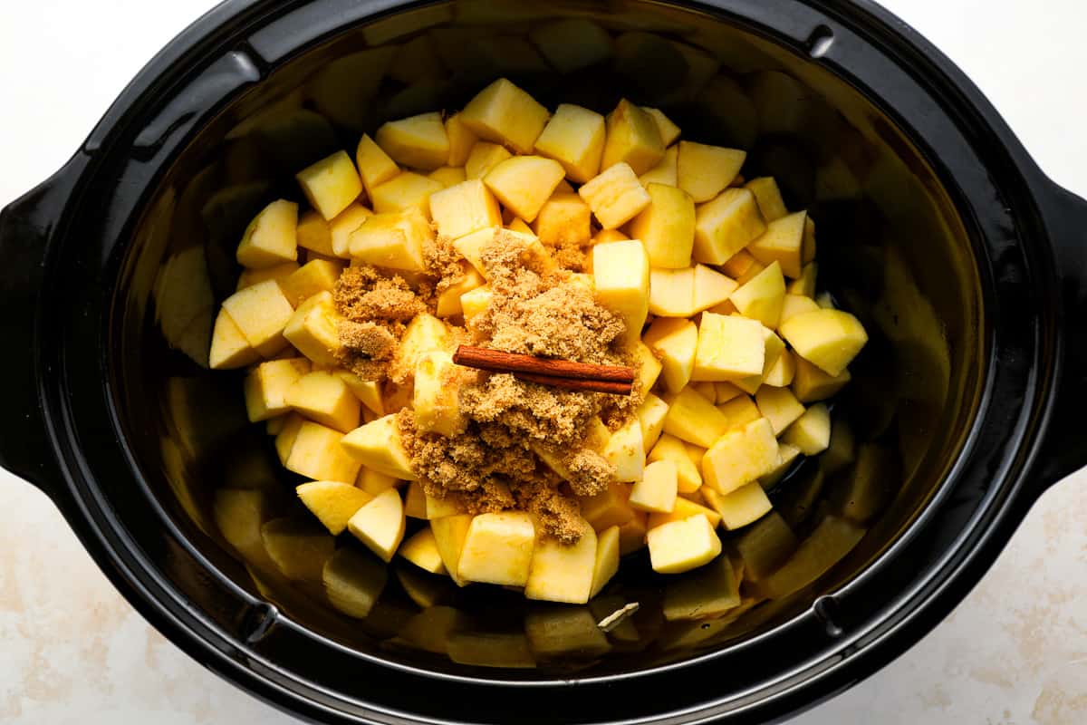 chopped apples topped with brown sugar and a cinnamon stick in a crockpot.