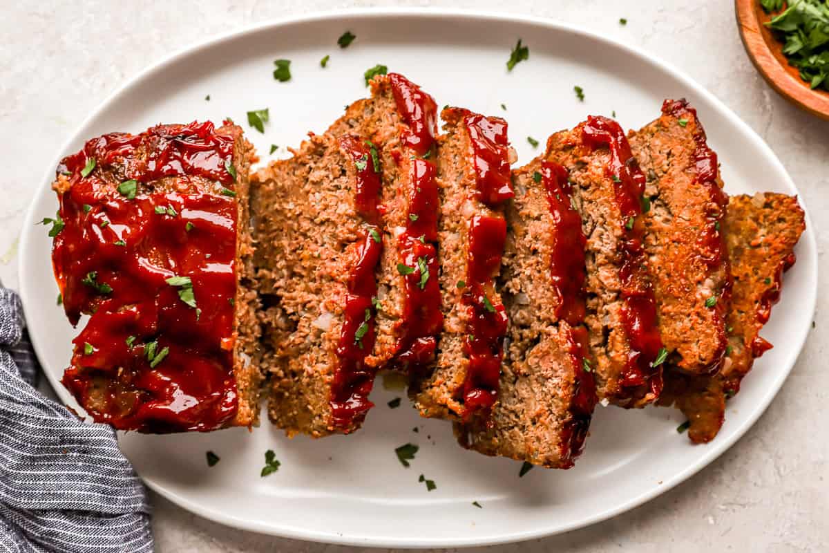 overhead view of a sliced meatloaf on a white platter.