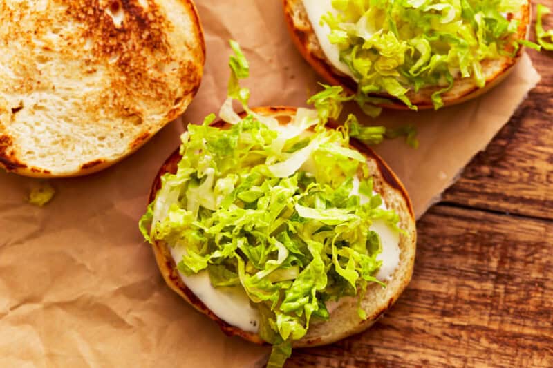 open hamburger buns topped with ranch dressing and shredded lettuce.