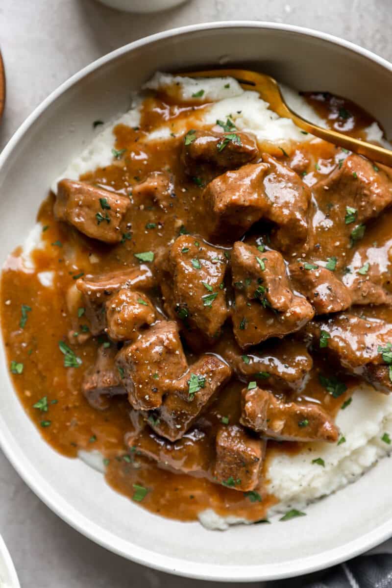 A bowl of beef tips and gravy served over mashed potatoes.