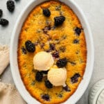 Baked blackberry cobbler in an oval baking dish, topped with ice cream and fresh berries.
