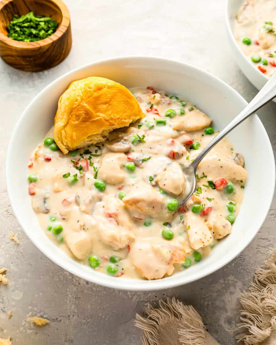 A bowl of creamy Chicken a la King, with a half-eaten biscuit on the side.