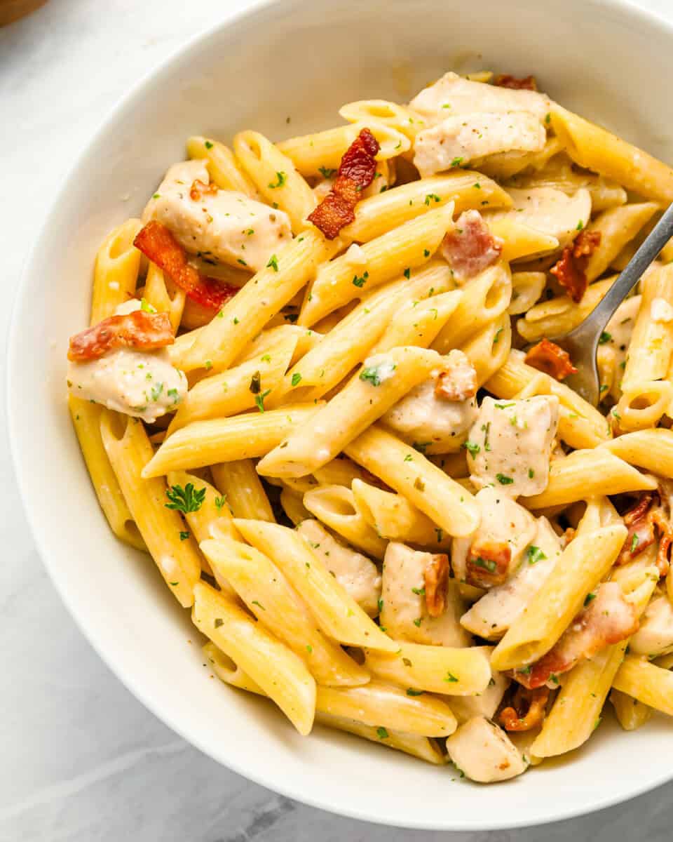 A bowl of penne pasta with chicken and bacon.