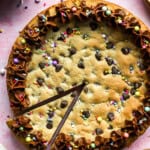 Homemade chocolate chip cookie cake with a triangular slice cut out.