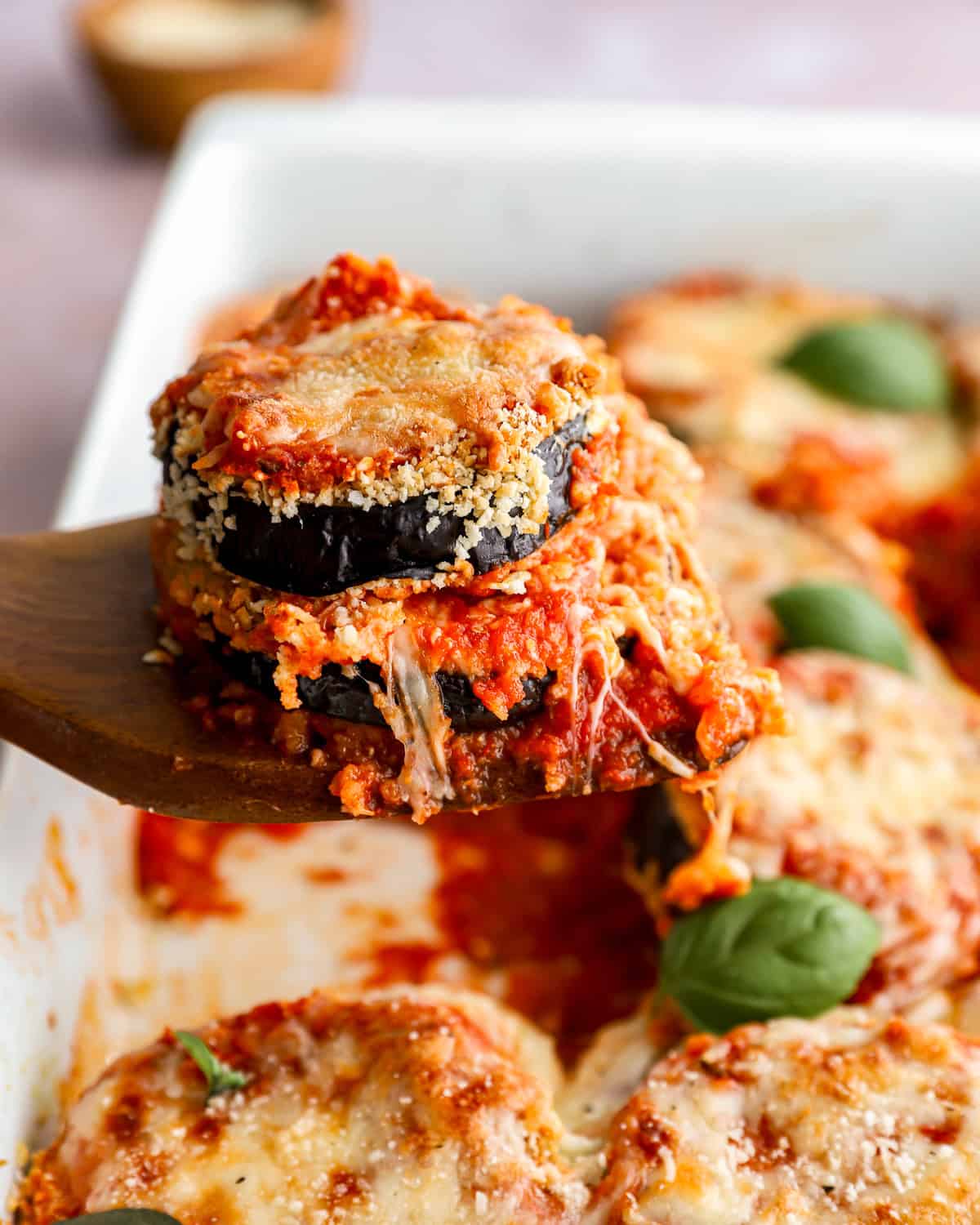 side view of a spatula removing a serving of eggplant parmesan from a baking pan.