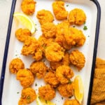 overhead view of fried shrimp on an enamel tray with lemon wedges.