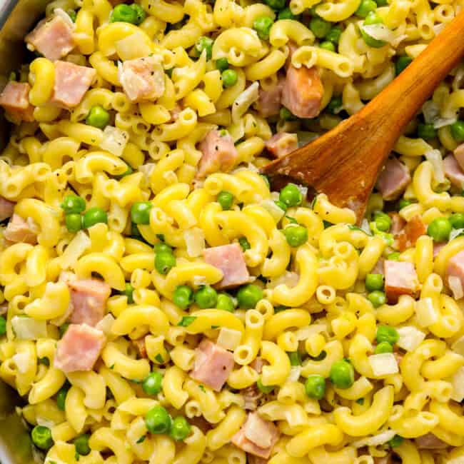 ham and pea pasta in a pot with a wooden spoon.