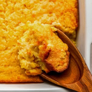 close up of a wooden spoon lifting a scoop of Jiffy corn casserole from a baking dish.