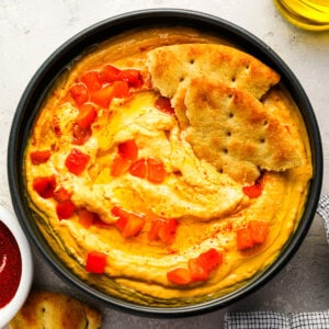 overhead view of roasted red pepper hummus with pepper pieces and pita bread.