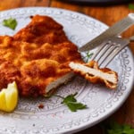 cut pork schnitzel on a plate with a fork and knife.