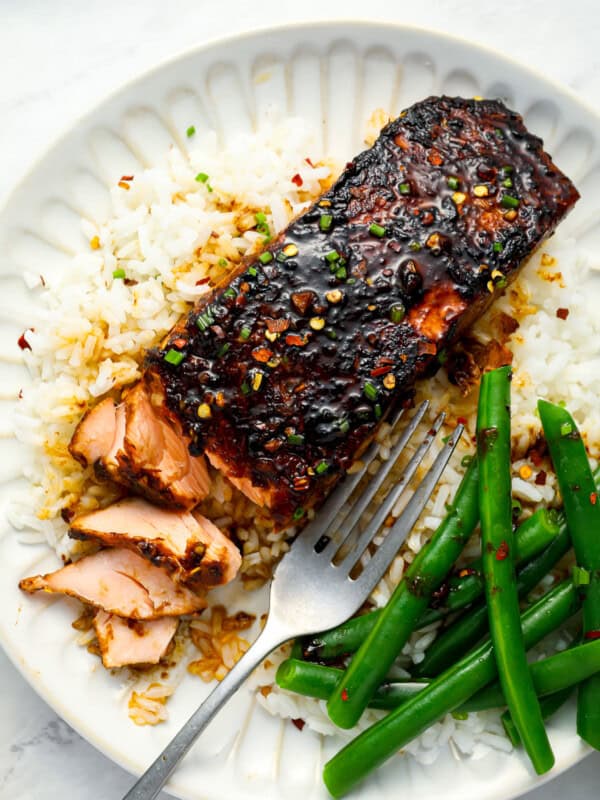 overhead view of a partially eaten serving of firecracker salmon on a white plate with green beans and a fork.