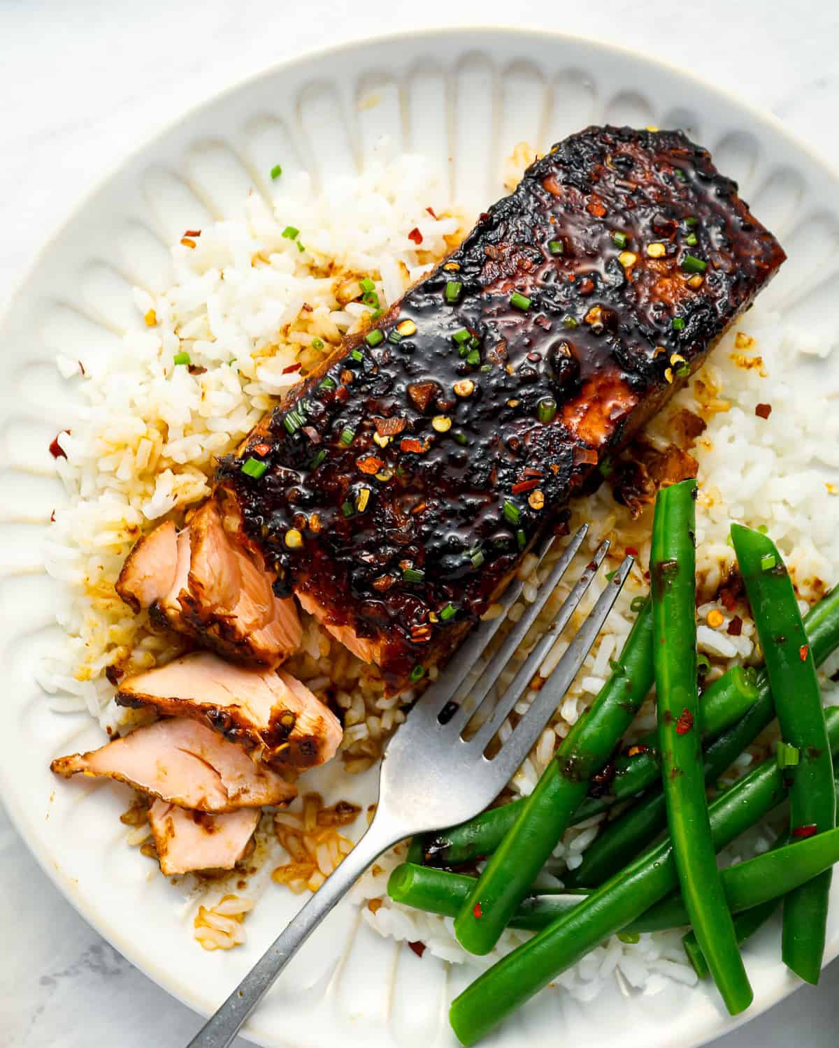 overhead view of a partially eaten serving of firecracker salmon on a white plate with green beans and a fork.