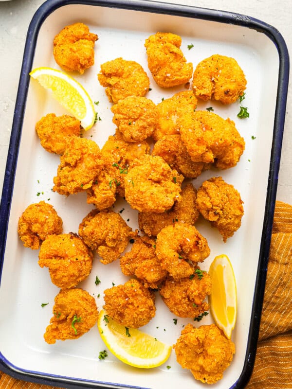 overhead view of fried shrimp on an enamel tray with lemon wedges.