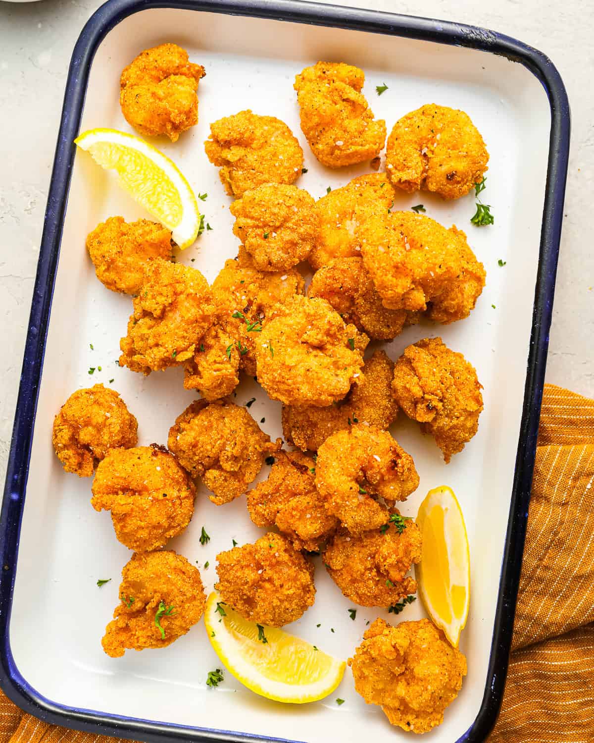 overhead view of fried shrimp on an enamel tray with lemon wedges.