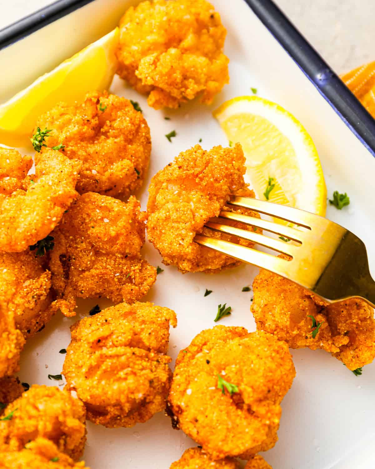 a fork stabbing a fried shrimp on an enamel tray.