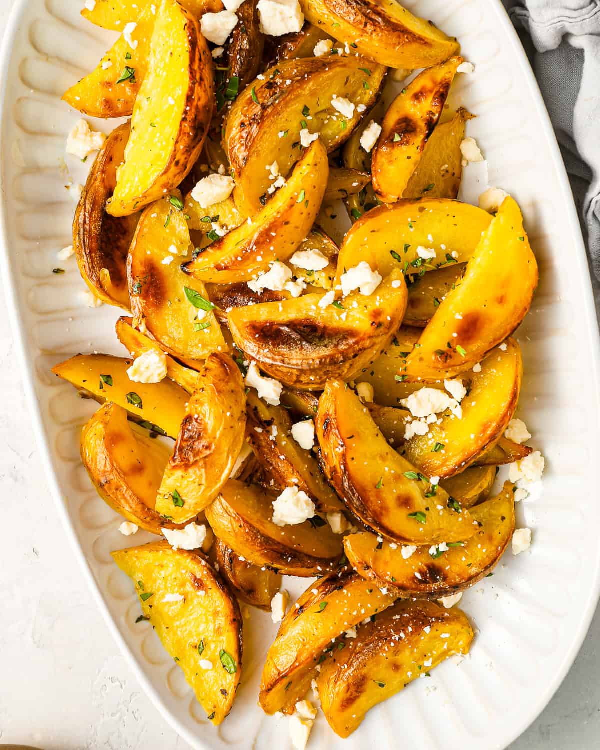 overhead view of greek potatoes topped with feta on a serving platter.