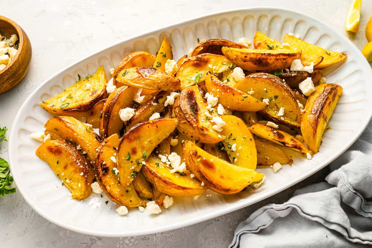 greek potatoes topped with feta on a serving platter.