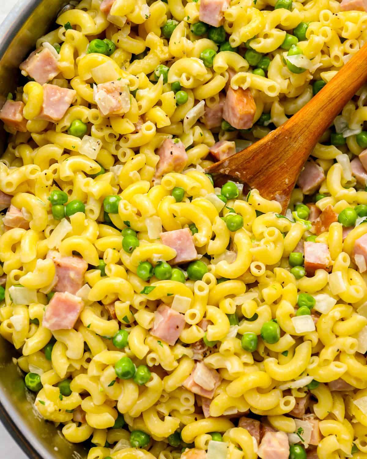 ham and pea pasta in a pot with a wooden spoon.