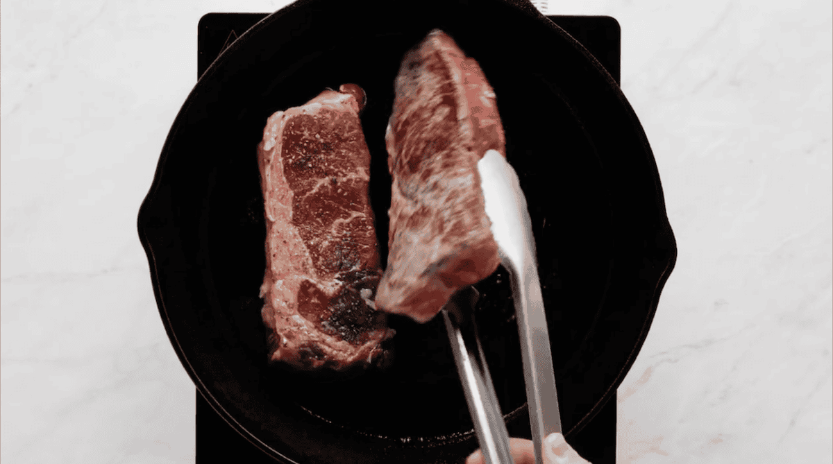 Flipping steaks over in a cast iron skillet.