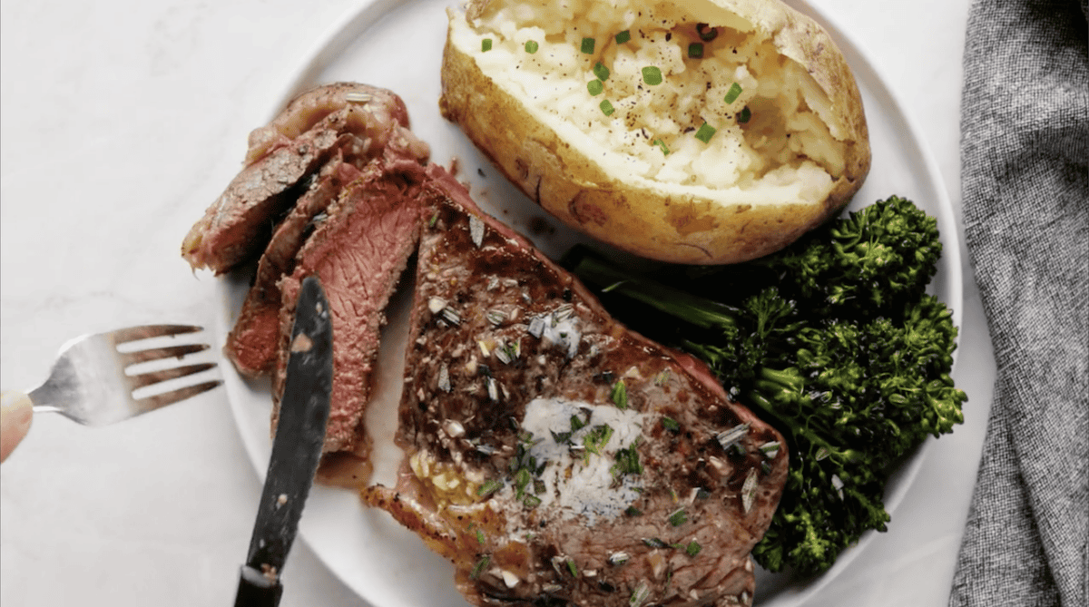 slicing a ribeye steak, on a plate with broccoli and a baked potato.