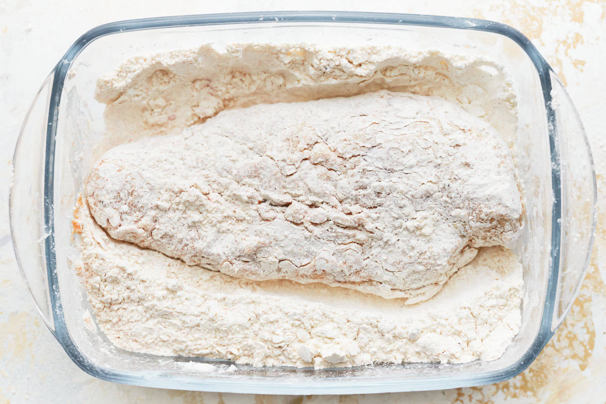 chicken coated in flour in a glass dish.