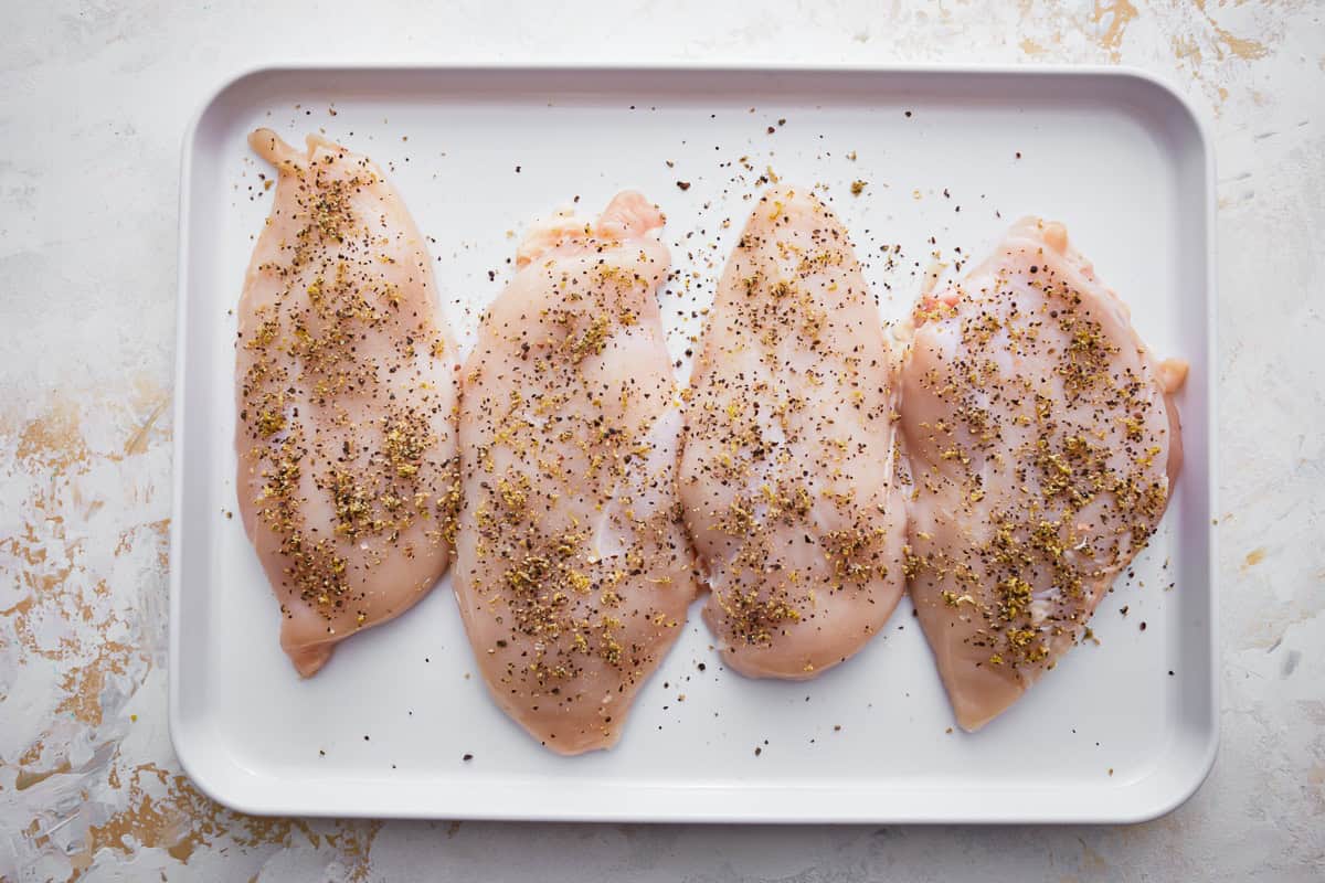 seasoned raw chicken breasts on a sheet pan.