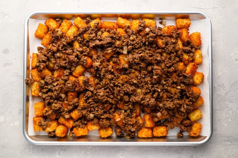 cooked ground beef over tater tots on a baking sheet.