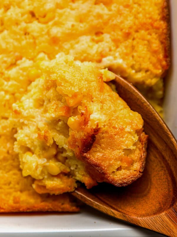 close up of a wooden spoon lifting a scoop of Jiffy corn casserole from a baking dish.