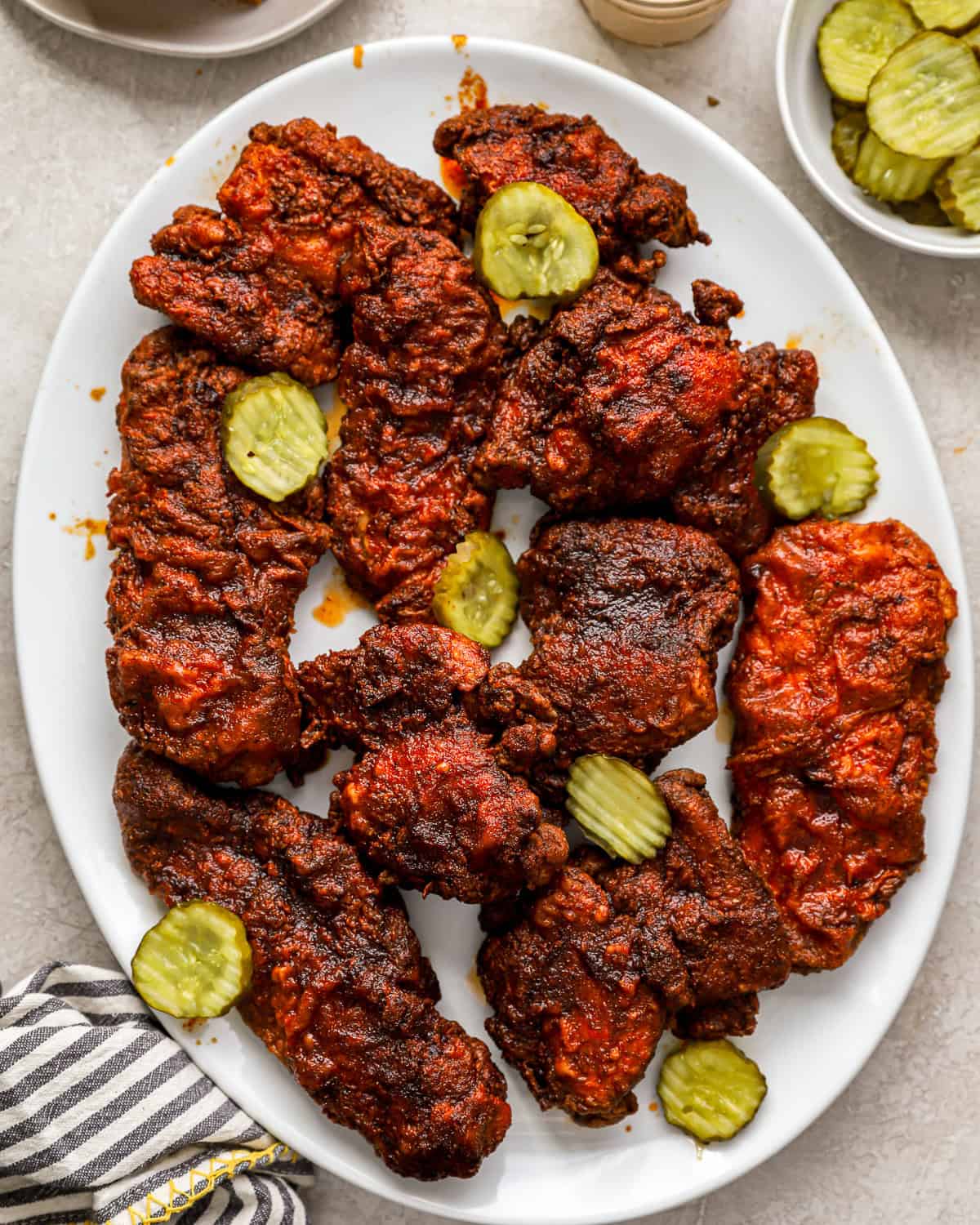 overhead view of nashville hot chicken on a white serving platter with pickles.