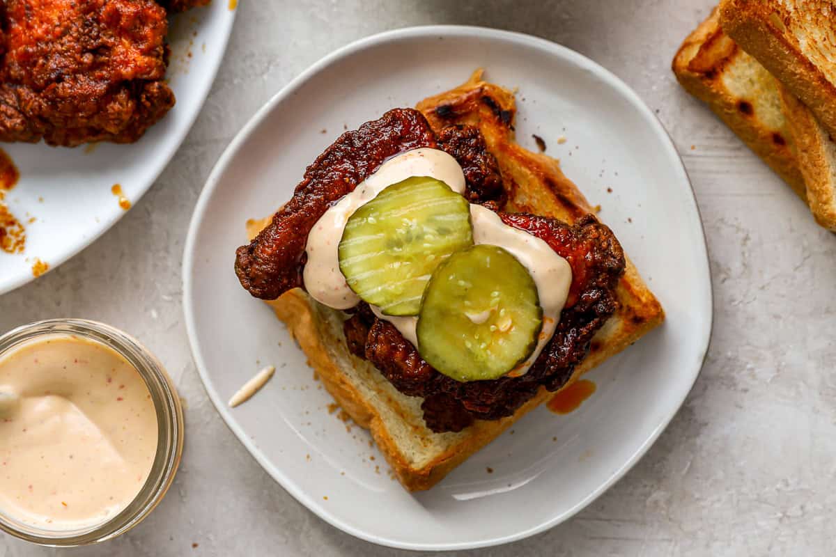 a piece of nashville hot chicken on texas toast topped with mayonnaise and pickles.