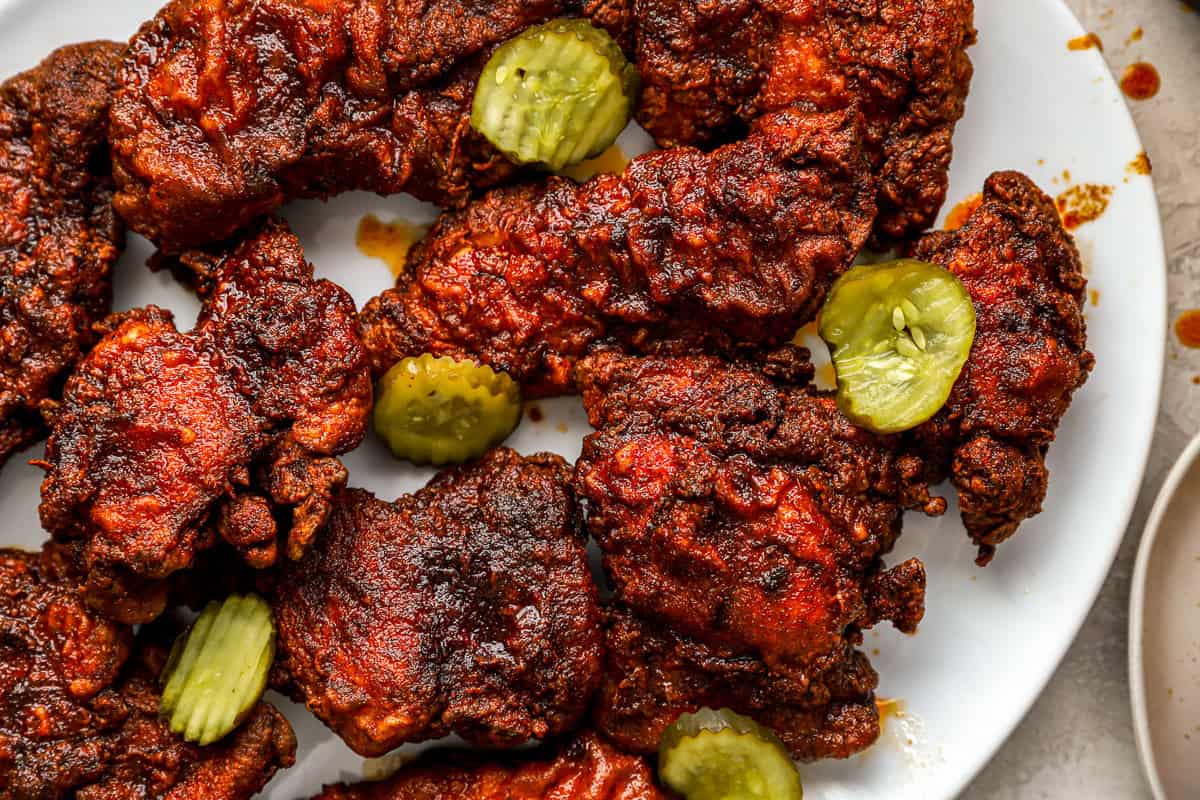 close up of nashville hot chicken on a white platter with pickles.