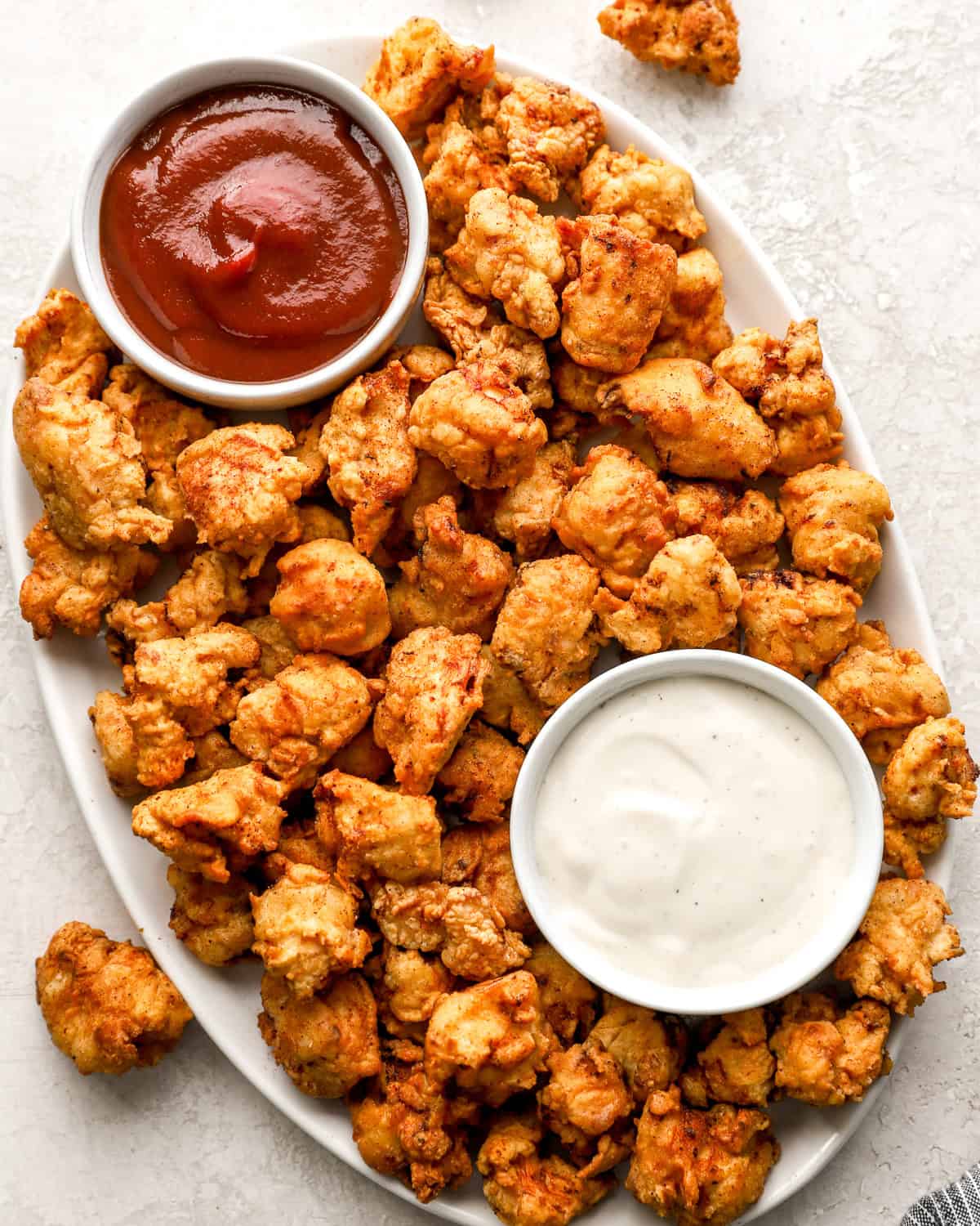 overhead view of popcorn chicken on a serving platter with mayo and ketchup.