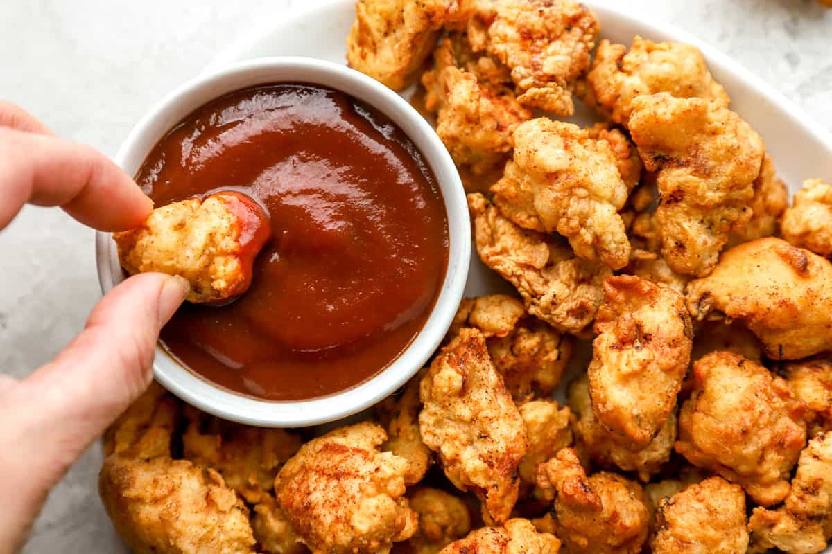 dipping a piece of popcorn chicken into ketchup.