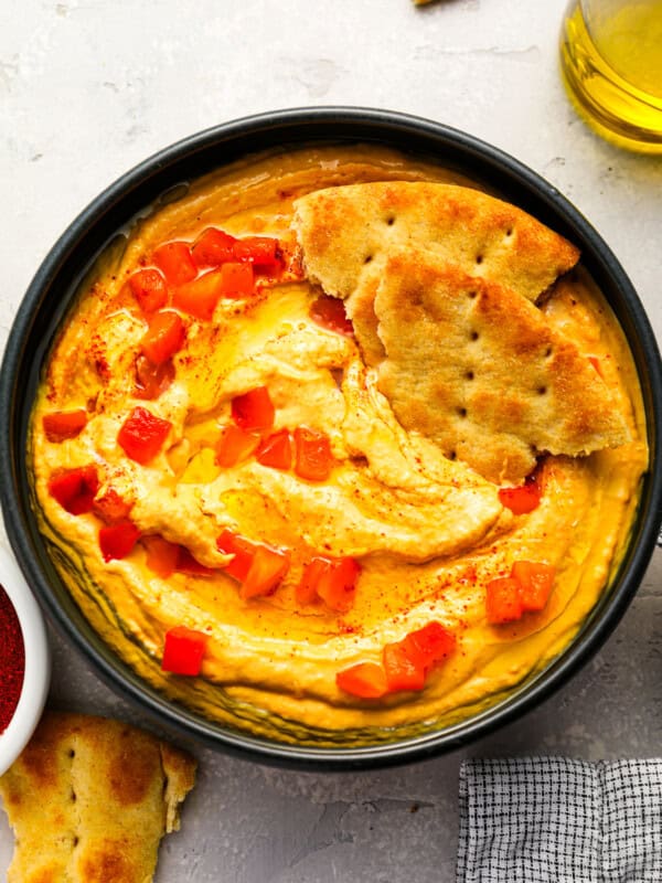 overhead view of roasted red pepper hummus with pepper pieces and pita bread.