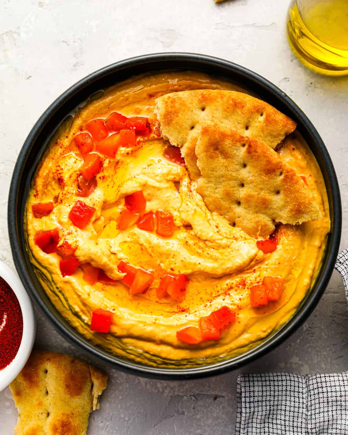 overhead view of roasted red pepper hummus with pepper pieces and pita bread.