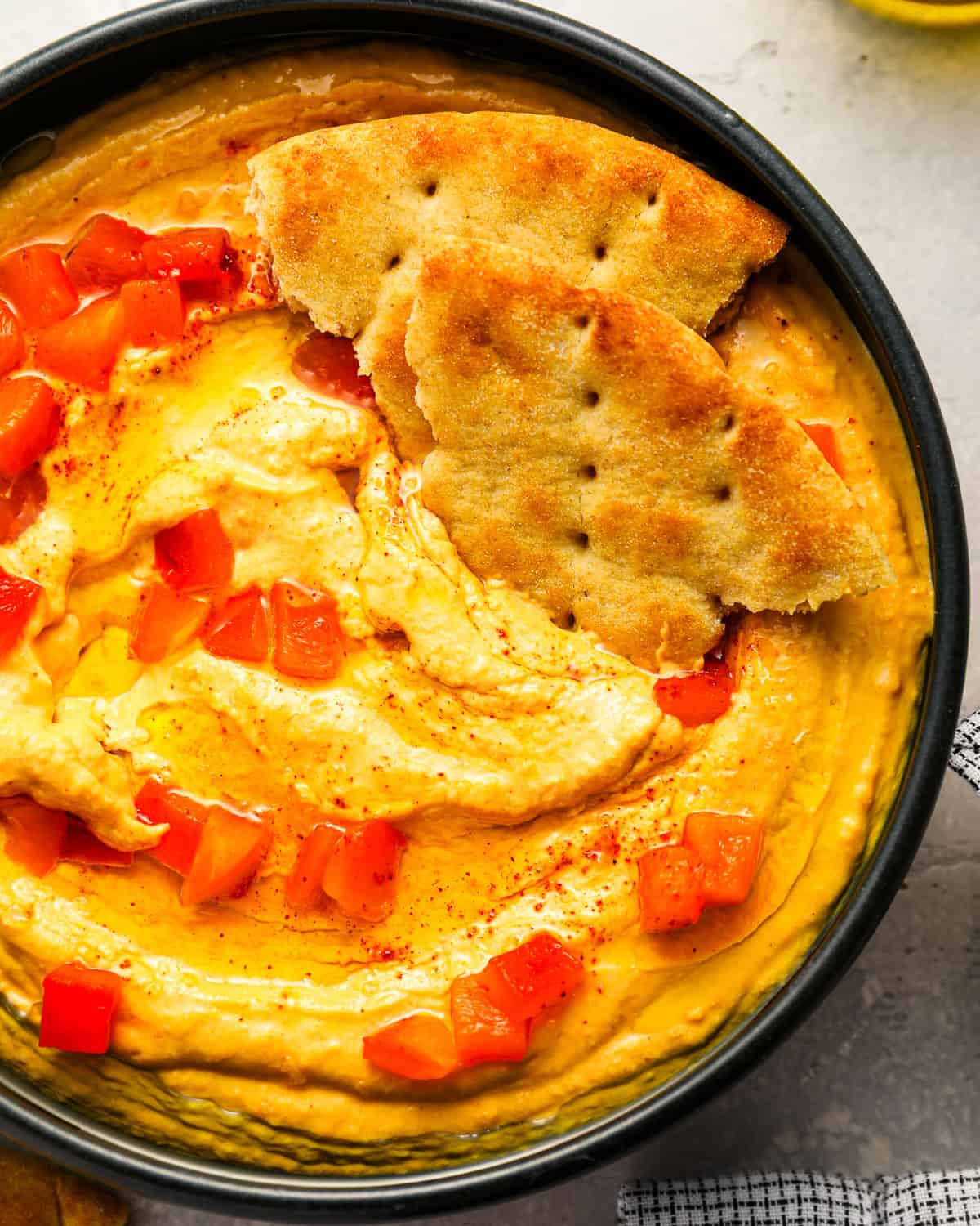 close up view of roasted red pepper hummus with pepper pieces and pita bread.