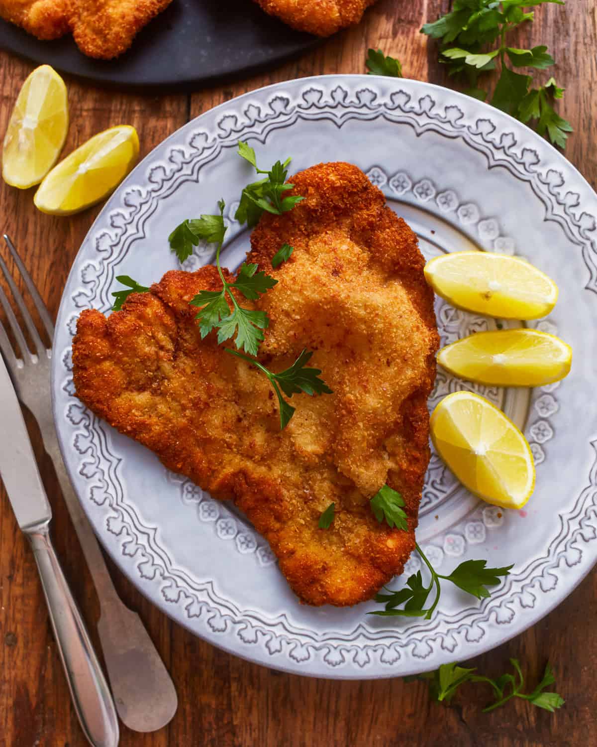 overhead view of a serving of pork schnitzel on a plate with lemon wedges.