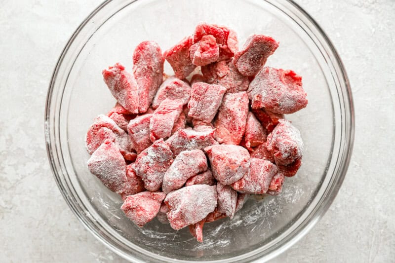 Raw beef tips coated in flour, in a glass mixing bowl.