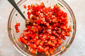A mix of tomatoes, garlic, and basil in a glass mixing bowl.
