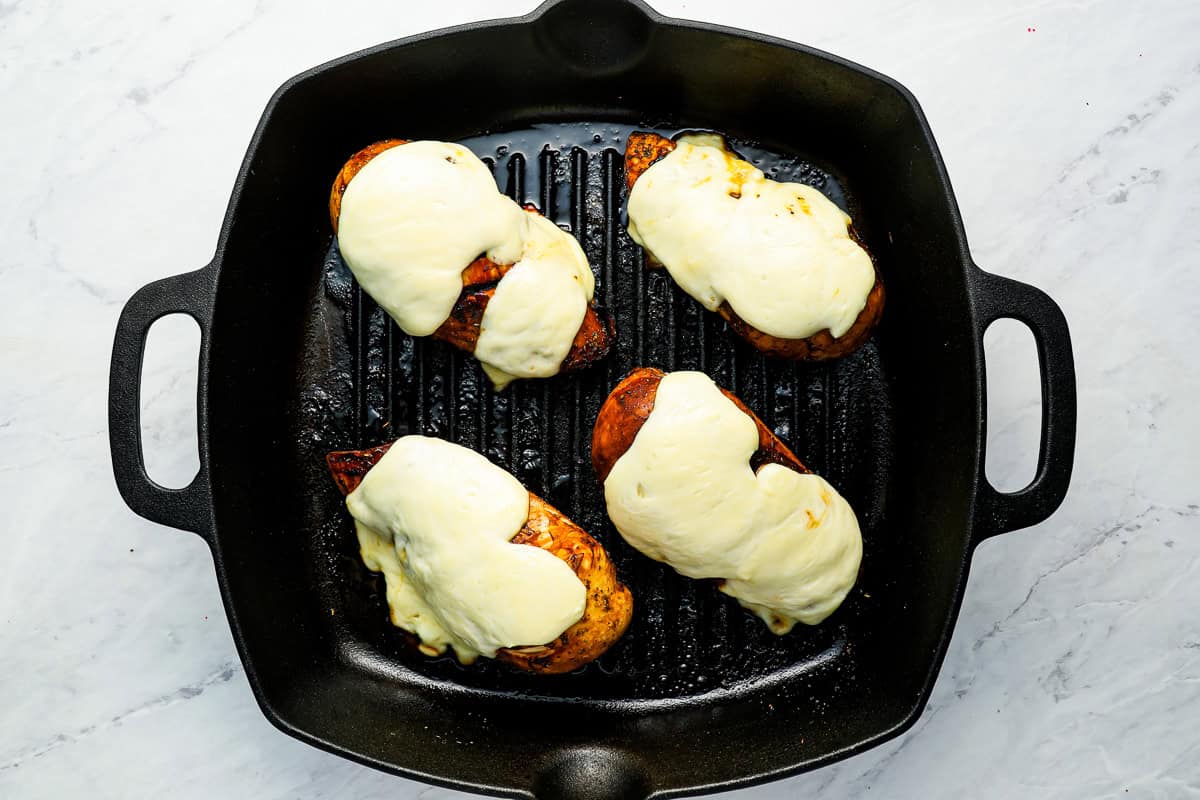 Chicken breasts topped with mozzarella, cooking in a grill pan.