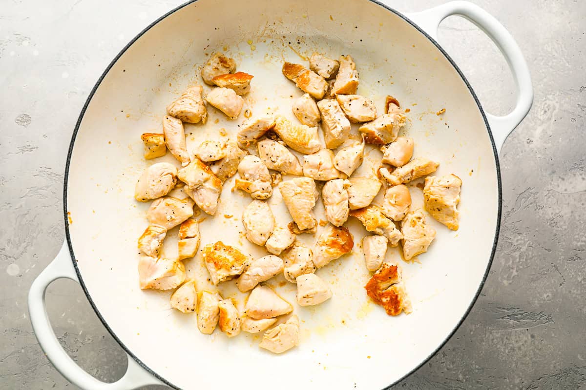 Small pieces of chicken cooking in a Dutch oven.