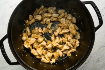 Bites of chicken cooking in a Dutch oven.