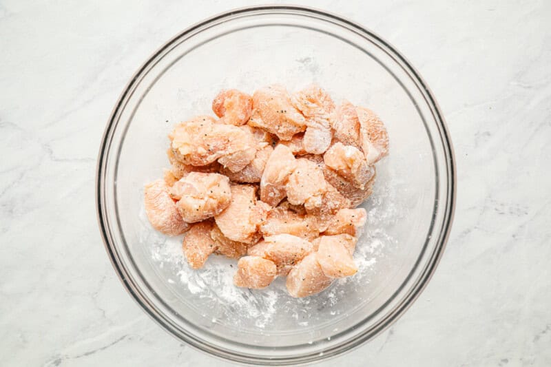 Bite-sized pieces of uncooked chicken combined with seasonings in a mixing bowl.