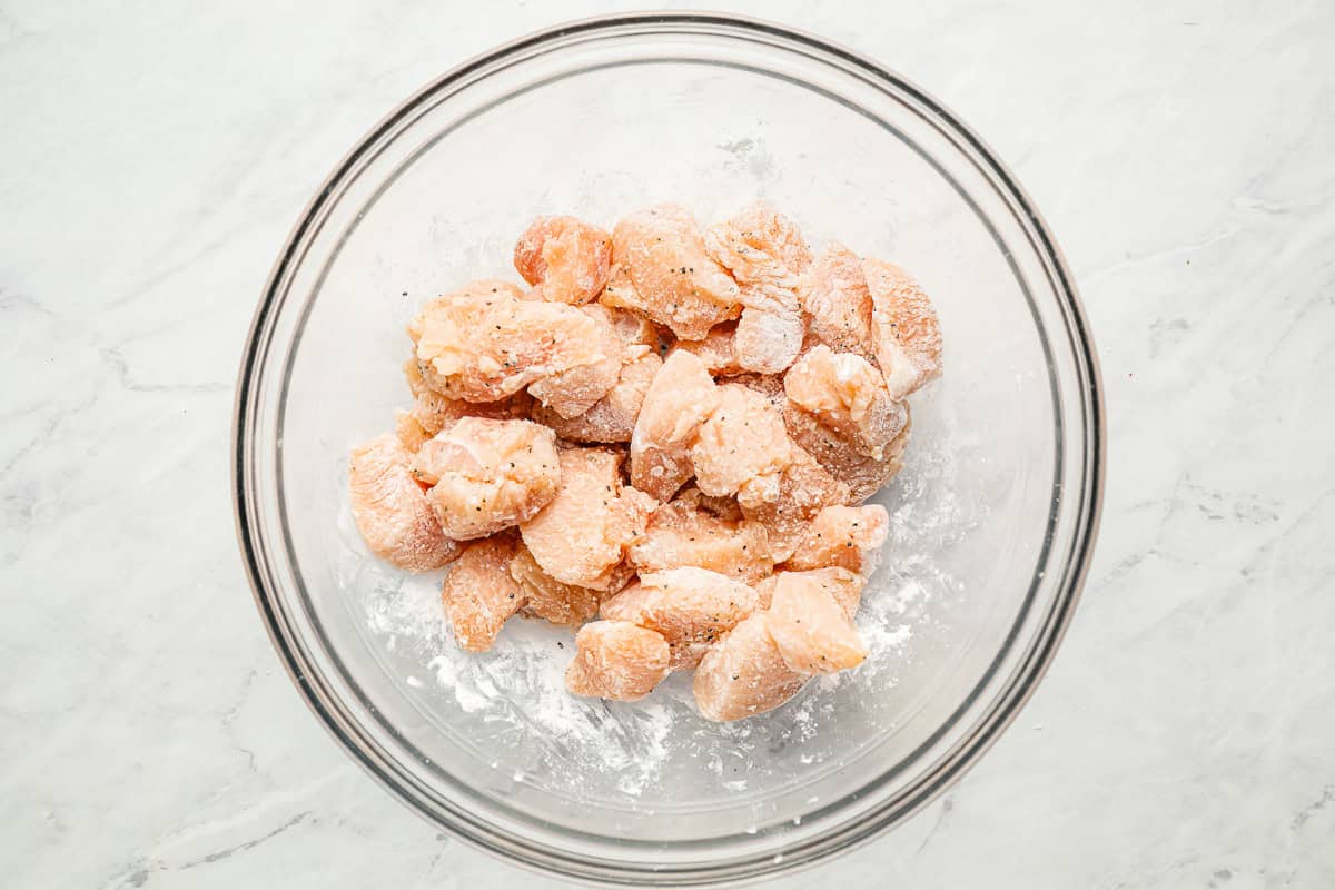 Bite-sized pieces of uncooked chicken combined with cornstarch in a mixing bowl.
