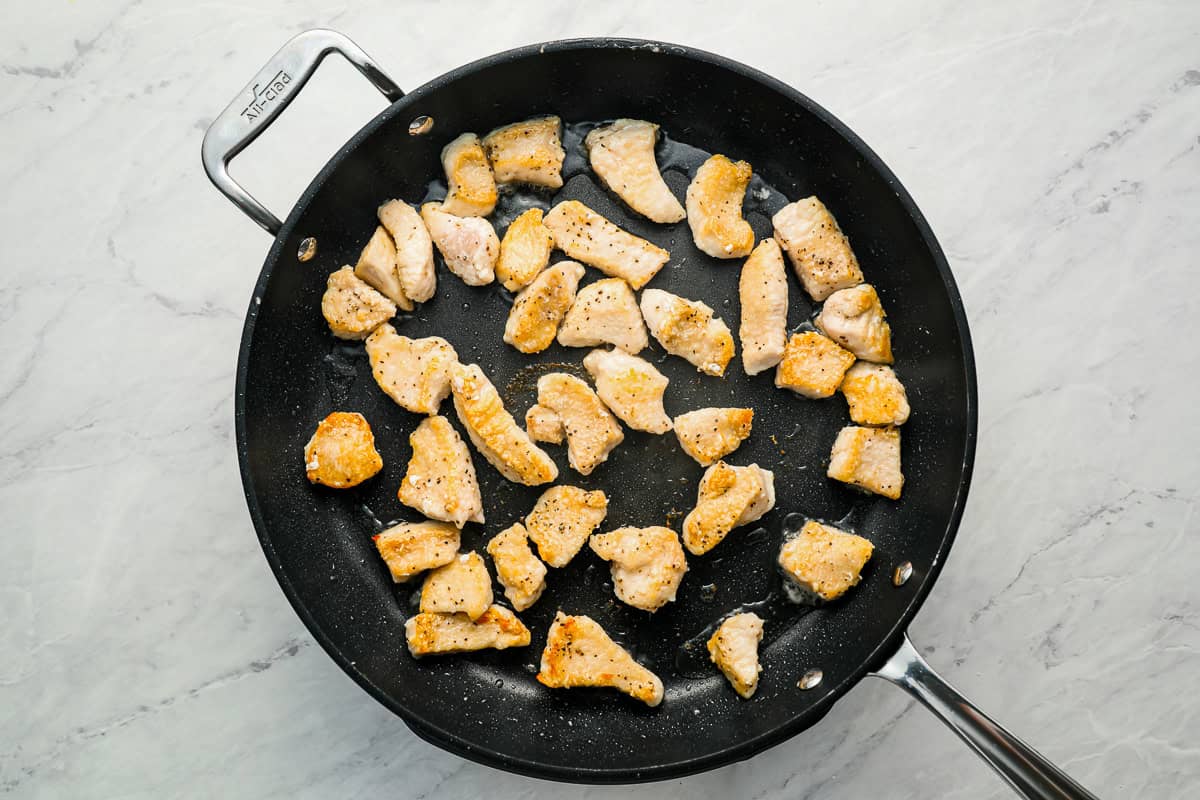 Small pieces of chicken breast cooking in a skillet.