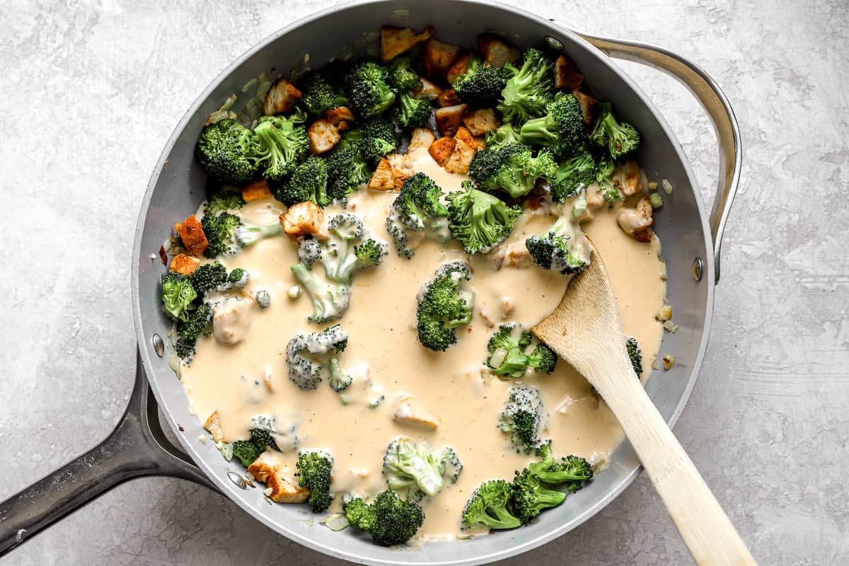 Broccoli and bites of chicken cooking in a cream sauce, in a skillet.