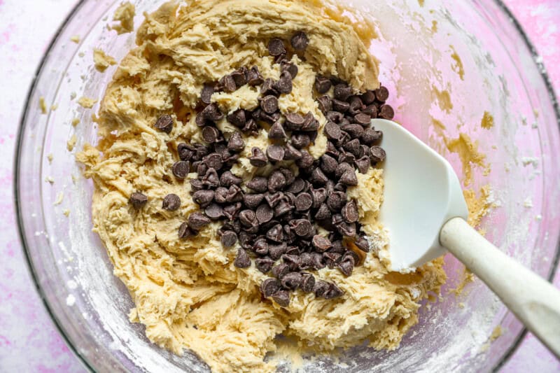 Rubber spatula folding chocolate chips into cookie dough.